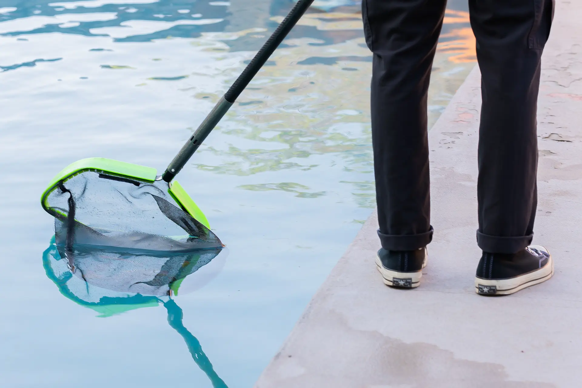 A Murdock Pool Service technician skimming the surface of a customer pool